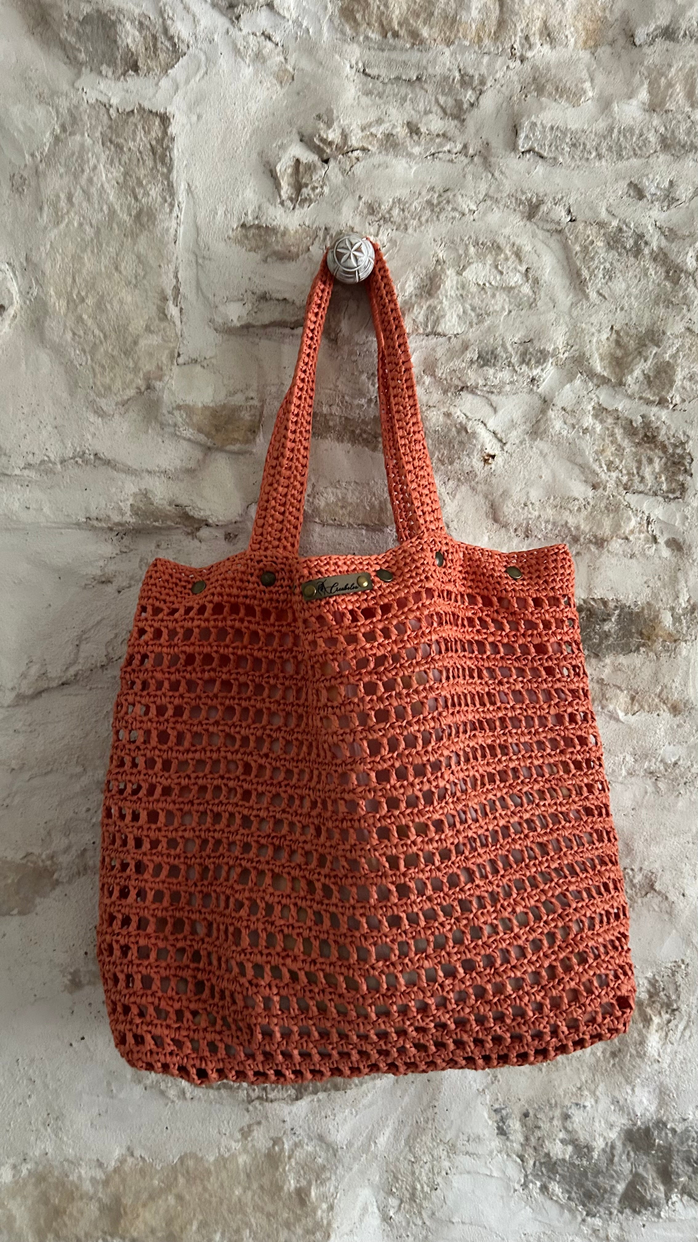 Sac cabas bohème en crochet corail détail suspendu mur pierre
